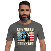 4th of July T-shirt with '100% American Drunkard' text, man drinking a bottle of beer wearing a trucker hat, and distressed American flag background