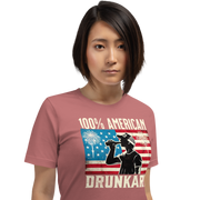4th of July T-shirt with '100% American Drunkard' text, man drinking a bottle of beer wearing a trucker hat, and distressed American flag background