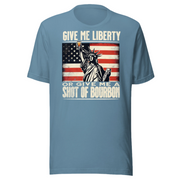 T-shirt with Give Me Liberty or Give Me a Shot of Bourbon text, Statue of Liberty holding a shot glass, and distressed American flag background. Perfect for 4th of July.
