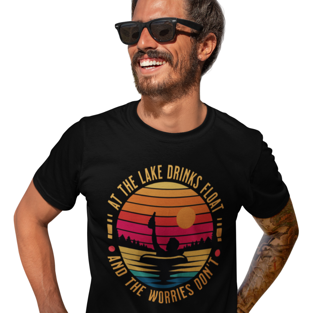 a man wearing a black tee with the phrase at the lake the drinks float and the woriees don't featuring a man in a floatie drinking beer with a retro sunset in the background