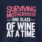 a navy sweatshirt with the phrase 'Surviving Motherhood One Glass of Wine at a Time' funny mother's day, mom life, girls trip design