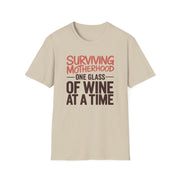 a beige t-shirt with the phrase 'Surviving Motherhood One Glass of Wine at a Time' funny Mother's day, beach vacation, spring break design