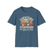 a light blue black t-shirt with the phrase 'Surviving Fatherhood One Beer at a Time" and a retro sunset graphic of a man drinking a beer funny father's day dad gift idea