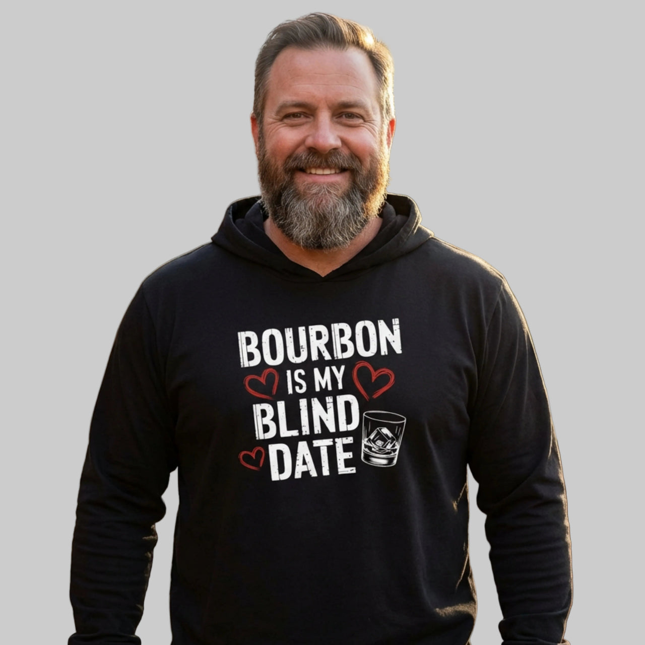 Man wearing a black hoodie with 'Bourbon is my blind date' text on a wooden deck.