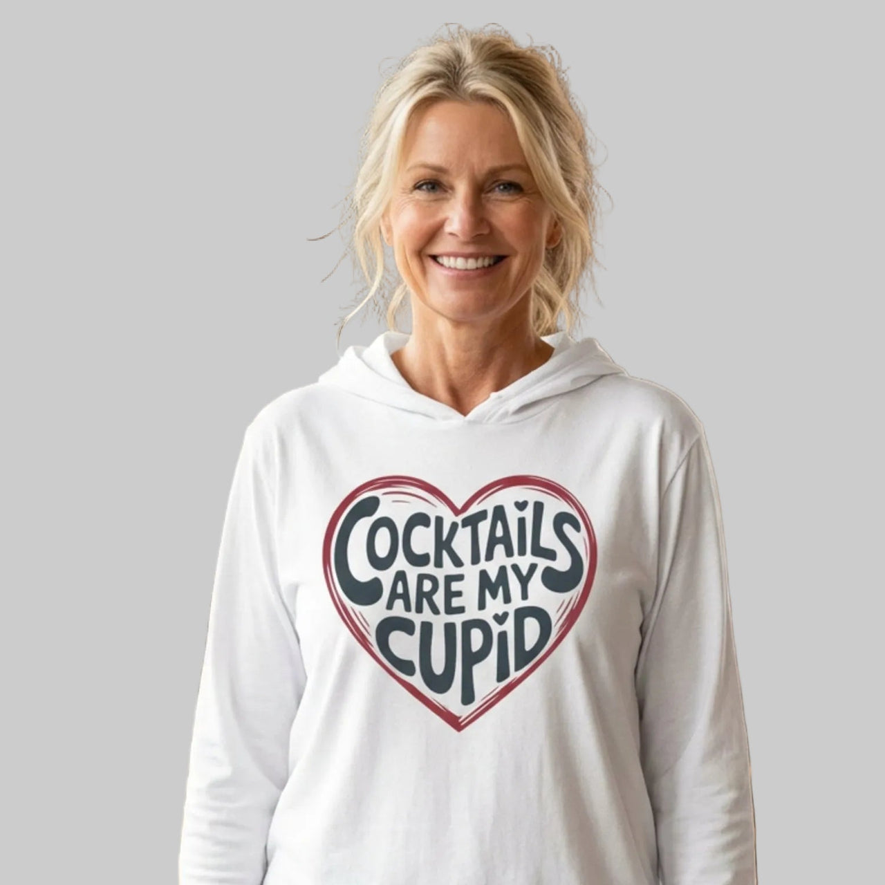blonde female model wearing white  featherweight hoodie with the phrase "Cocktails are my cupid".  A minimalist valentine heart outline surrounds the phrase to complete the design
