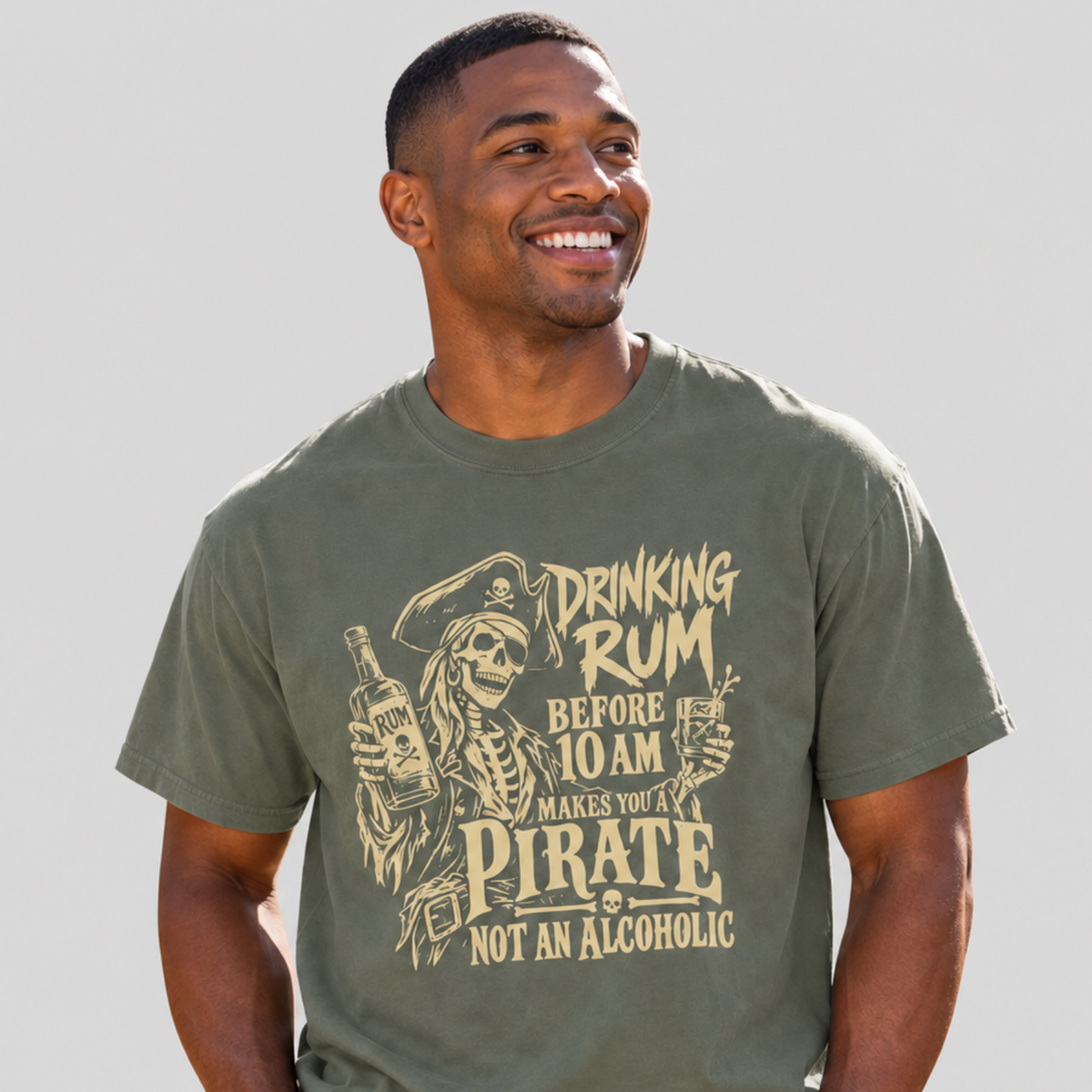 A man wearing an olive green graphic t-shirt with a pirate-themed design and text that reads 'DRINKING RUM BEFORE 10 AM MAKES YOU A PIRATE NOT AN ALCOHOLIC'.