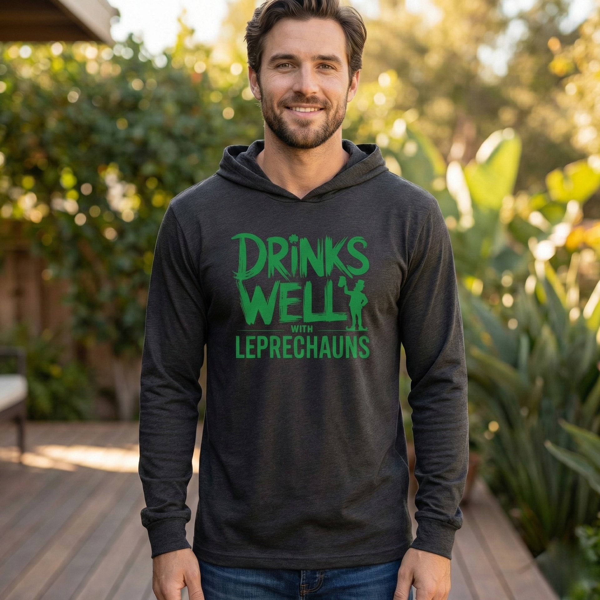 brunette male model wearing a black lightweight St Patricks  Day hoodie with the Phrase “Drinks Well With Leprechauns”  with a leprechaun to complete the design