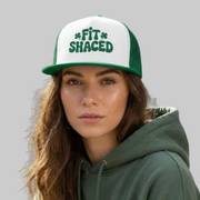 Person wearing a green and white cap with 'FITSHACED' text, sitting on a bench with graffiti in the background.