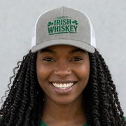 Woman wearing a gray and white curved trucker hat with the phrase 'Fueled by Irish Whiskey' funny St Patricks Day Pub crawl and parade design