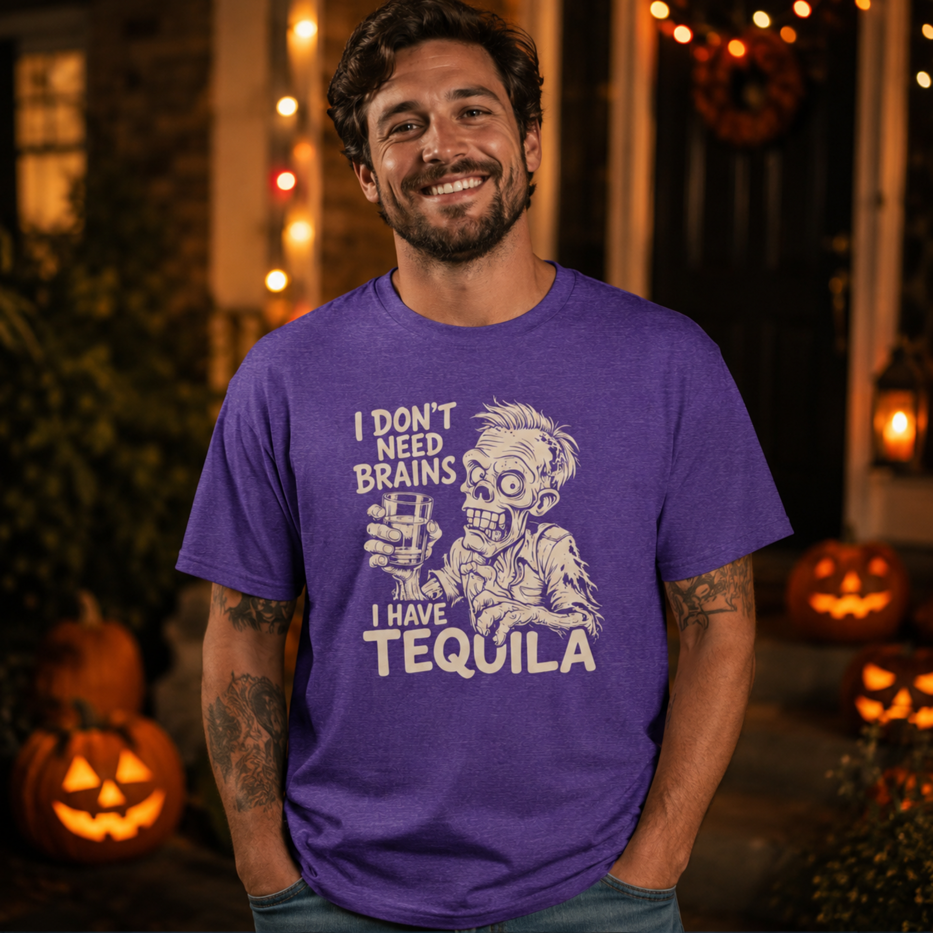 A man wearing a purple graphic t-shirt with a zombie holding a tequila glass and the text 'I DON'T NEED BRAINS I HAVE TEQUILA'. The background is a Halloween-themed outdoor setting with glowing jack-o'-lanterns and warm string lights.