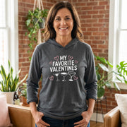 brunette female model wearing gray featherweight hoodie with the phrase "My Favorite Valentines".  Below the Phrase are three cocktail glasses. Minimalist Valentines Heart outlines surround the the phrase to complete the design
