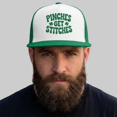 Man wearing a cap with 'Pinches Get Stitches' text against a brick wall.