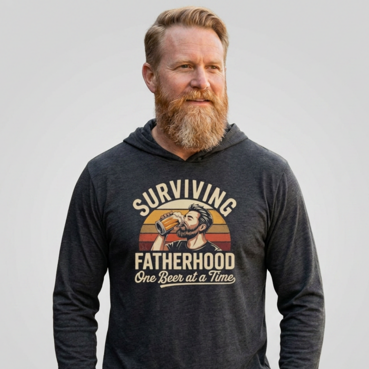 Man wearing a heather navy lightweight hoodie with the phrase 'Surviving Fatherhood One Beer at a Time' funny Father's day gift for dad