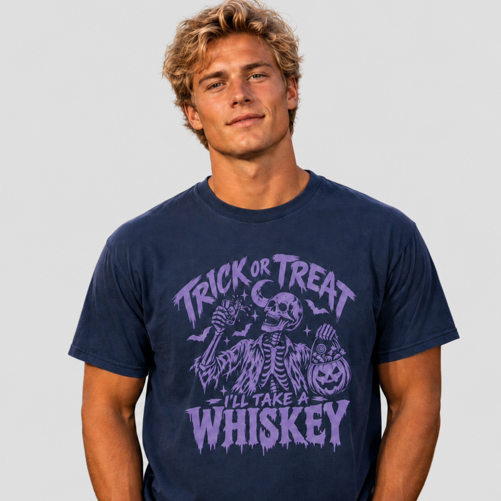 A man wearing a navy blue graphic t-shirt with a purple Halloween design that reads 'TRICK OR TREAT I'LL TAKE A WHISKEY'.