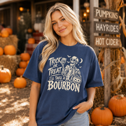 A woman wearing a navy blue graphic t-shirt with a white skeleton and text reading 'TRICK OR TREAT I'LL TAKE A BOURBON' in a rustic autumn setting with pumpkins and a 'Pumpkins Hayrides Hot Cider' sign.