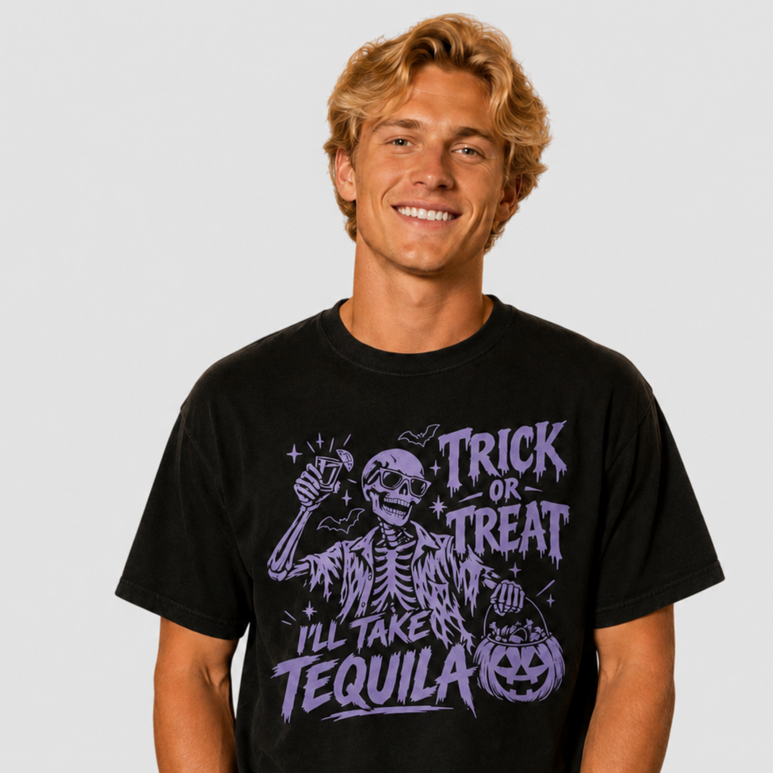 A smiling young man wearing a black graphic t-shirt with a purple 'Trick or Treat I'll Take Tequila' skeleton design, posed against a solid light gray background.