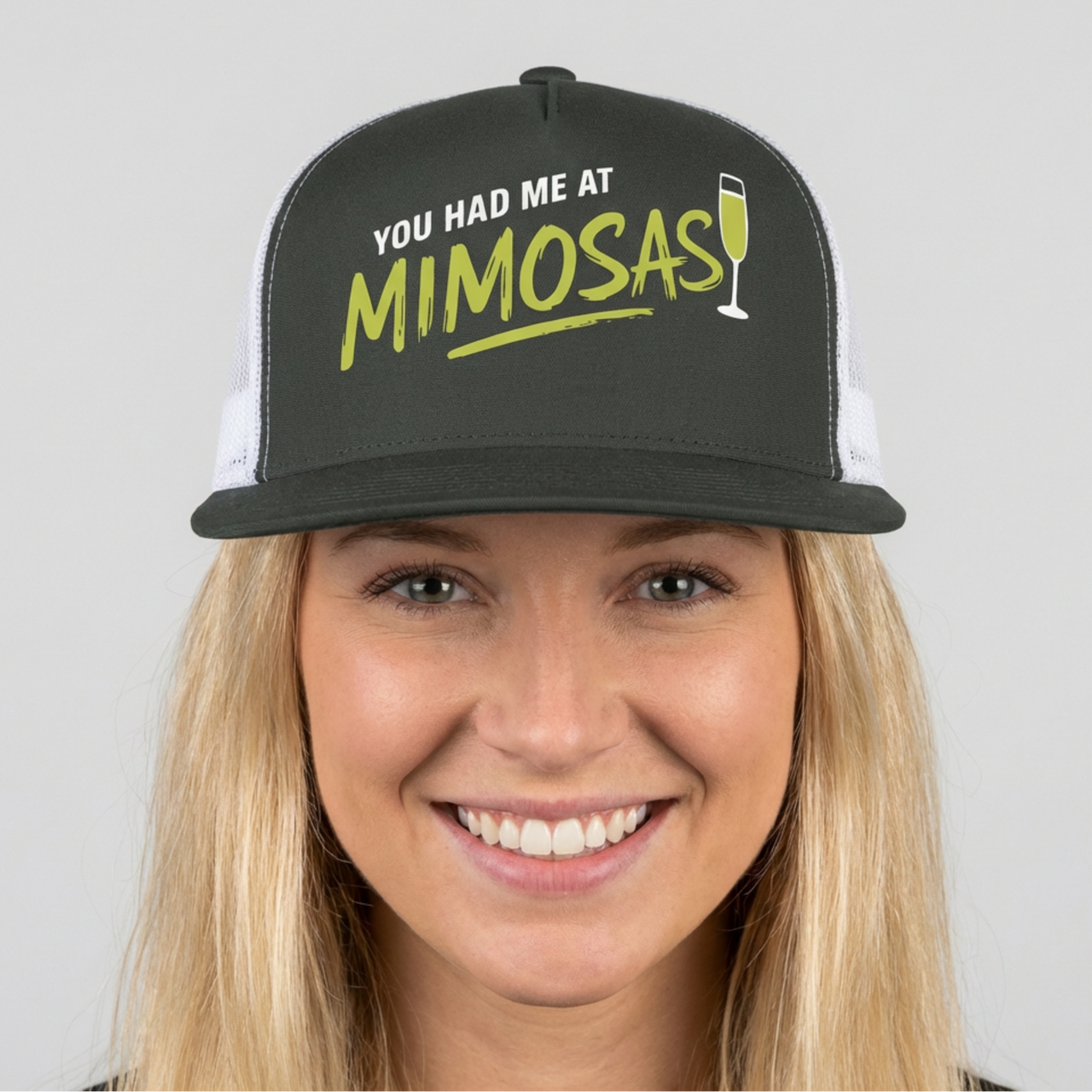 Woman wearing a charcoal and white flat bill trucker cap with 'You Had Me at Mimosas' text and champagne glass for Spring Break, Girls Trips, or Bachelorette Parties