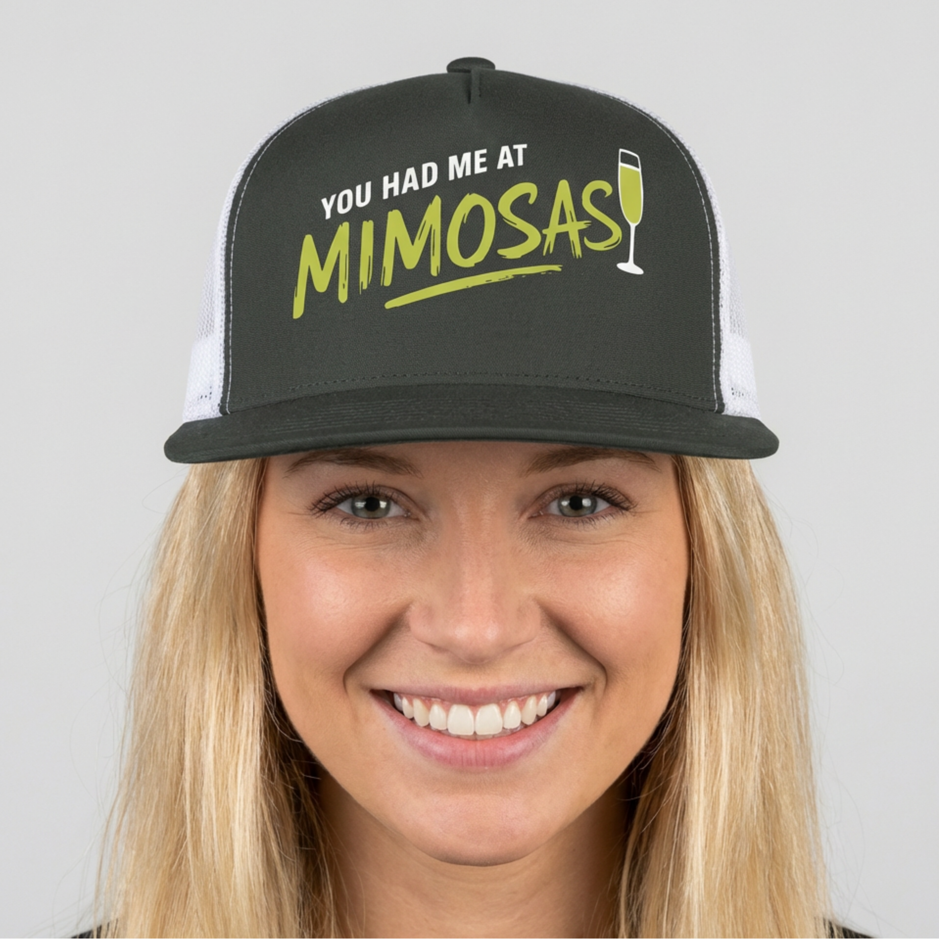 Woman wearing a charcoal and white flat bill trucker cap with 'You Had Me at Mimosas' text and champagne glass for Spring Break, Girls Trips, or Bachelorette Parties