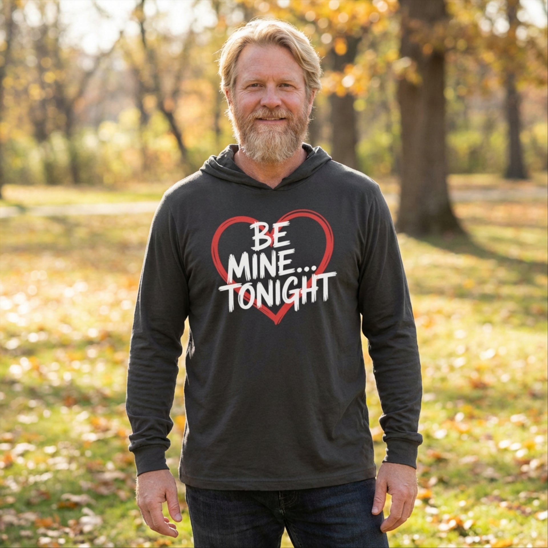 bearded blond male model wearingblack featherweight hoodie with the phrase "Be Mine... Tonight" with a minimalist sketched valentine's heart surrounding the phrase to complete the design
