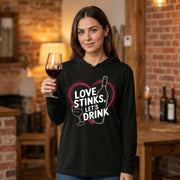 a brunette model wearing a black featherweight hoodie with the phrase "Love Stinks Let's Drink" surrounded by a sketched valentine's heart and a wine glass and wine bottle
