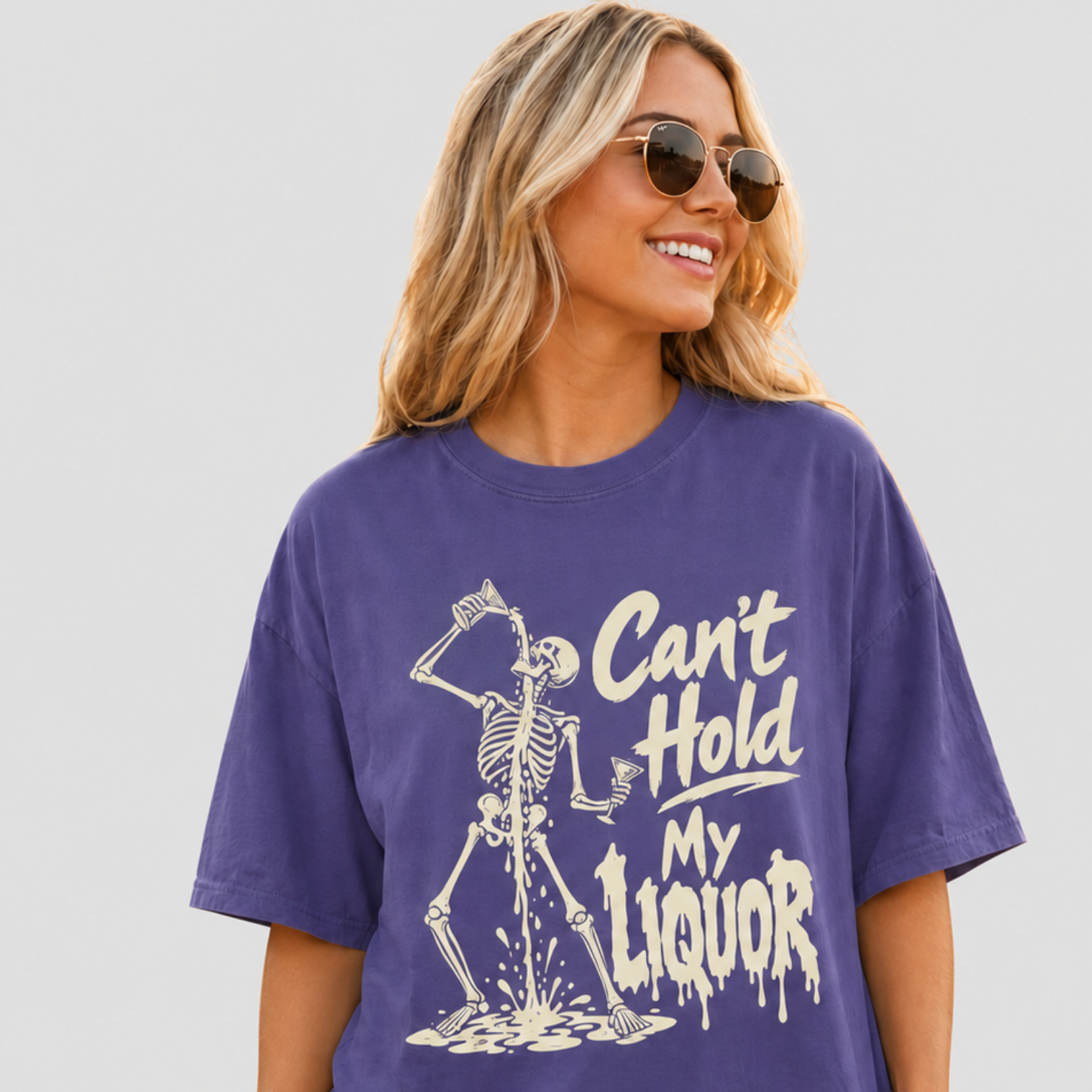 A woman wearing a purple graphic t-shirt with a white skeleton and the text 'Can't Hold My Liquor' on the front, paired with denim shorts and sunglasses, set against a solid light gray background.