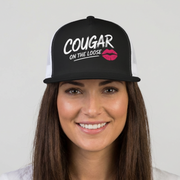 Woman wearing a black and white flat bill trucker hat with the phrase 'Cougar on the Loose' funny beach trip, girls trip, bachelorette party, or spring break design