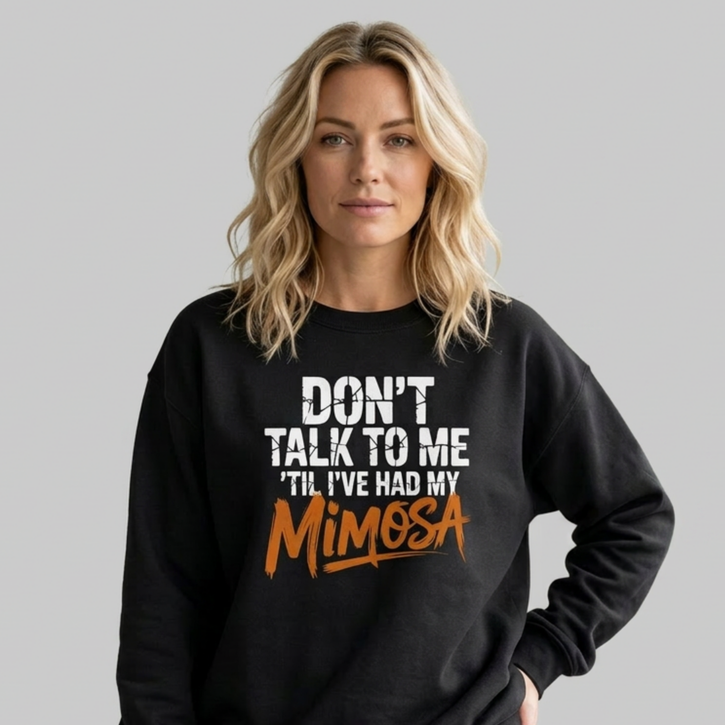 Woman wearing a black sweatshirt with the text 'Don't talk to me 'til i've had my mimosa'