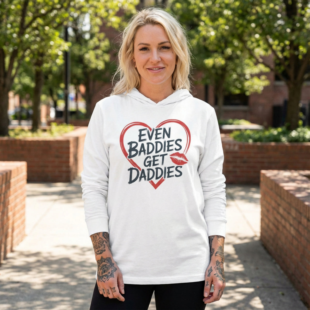 blonde female model wearing white featherweight hoodie with the phrase "Even Baddies Get Daddies" with a minimalist sketched valentine's heart surrounding the phrase to complete the design
