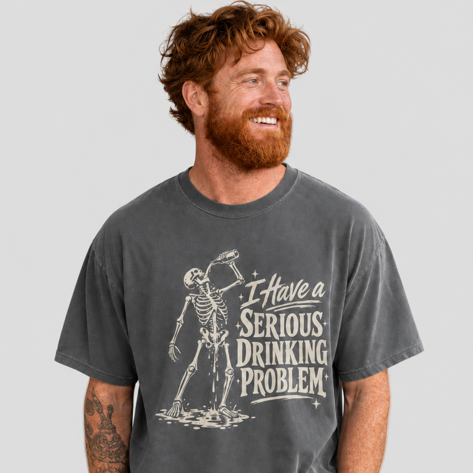 A man with red hair and a beard wearing a dark gray graphic t-shirt that reads 'I have a SERIOUS DRINKING PROBLEM' next to a skeleton holding a drink, set against a solid light gray background.