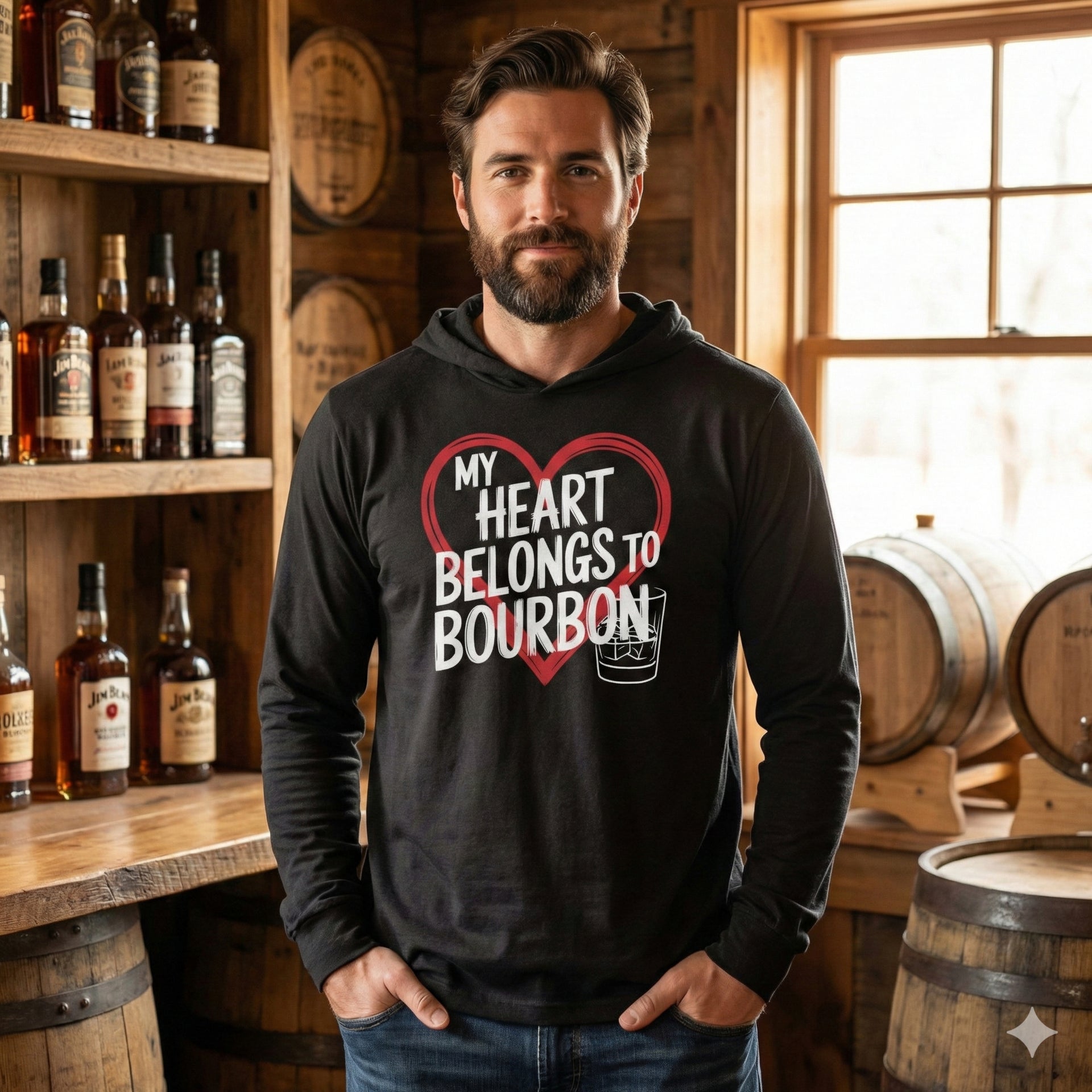 brunette male model wearing a black featherweight hoodie with the phrase “My “Heart Belongs to Bourbon” with an ink sketched heart surrounding the phrase and a bourbon glass to  complete the design