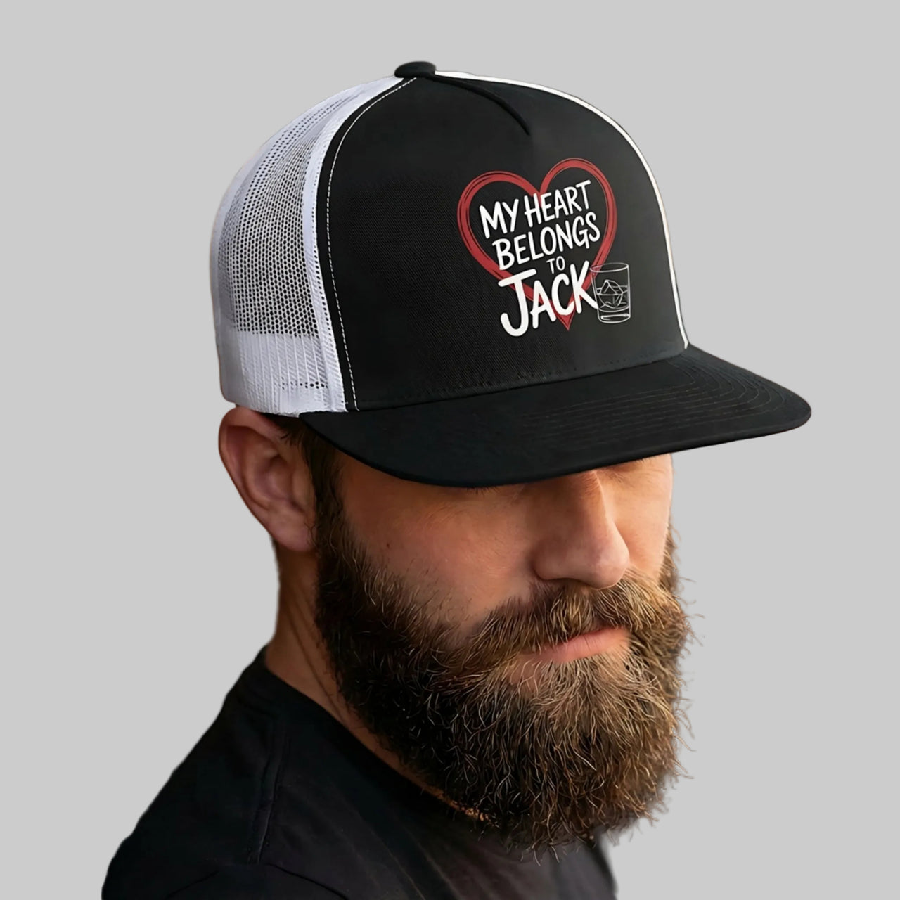 Man wearing a black and white cap with 'My Heart Belongs to Jack' text, leaning against a wooden wall.