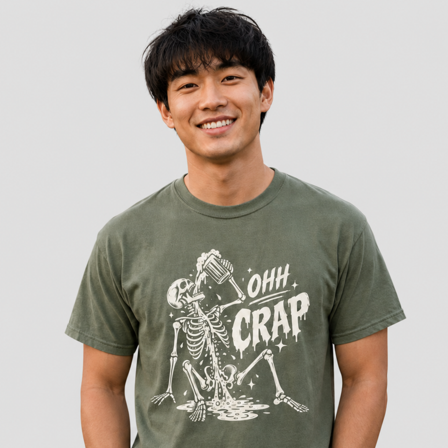 A smiling man wearing an olive green crewneck t-shirt with a white graphic of a skeleton drinking beer and the text 'OHH CRAP'.
