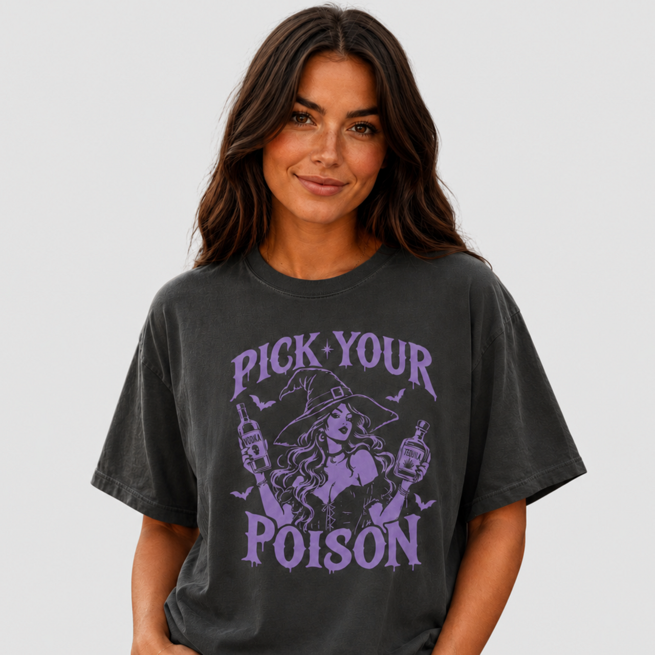 A woman wearing a faded black graphic t-shirt with a purple 'PICK YOUR POISON' witch design, paired with light wash jeans, against a solid light gray background.