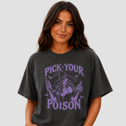A woman wearing a faded black graphic t-shirt with a purple 'PICK YOUR POISON' witch design, paired with light wash jeans, against a solid light gray background.