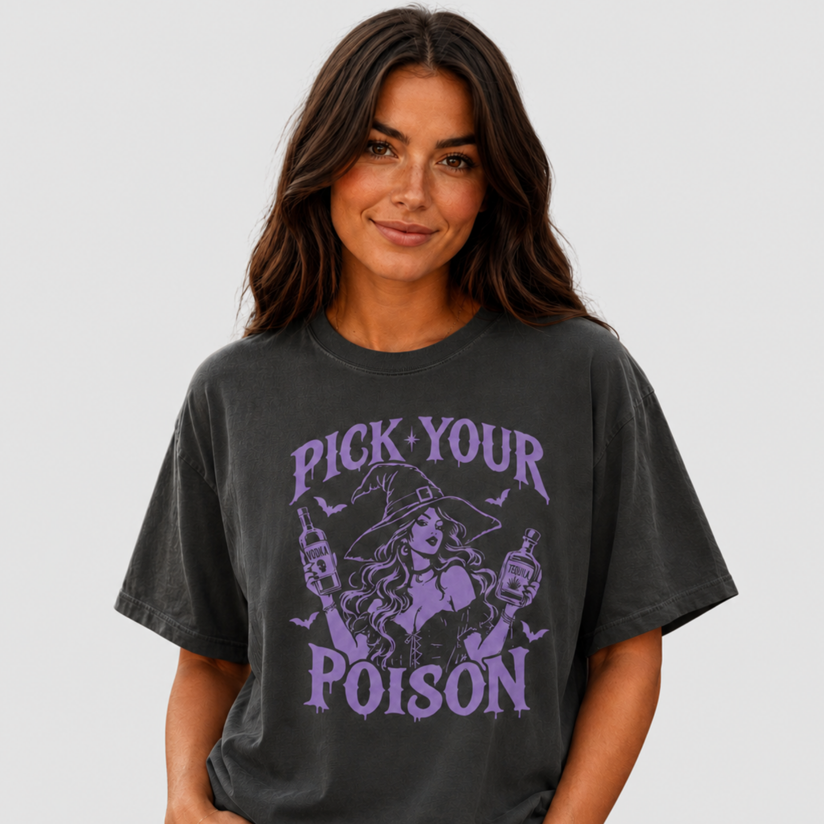 A woman wearing a faded black graphic t-shirt with a purple 'PICK YOUR POISON' witch design, paired with light wash jeans, against a solid light gray background.