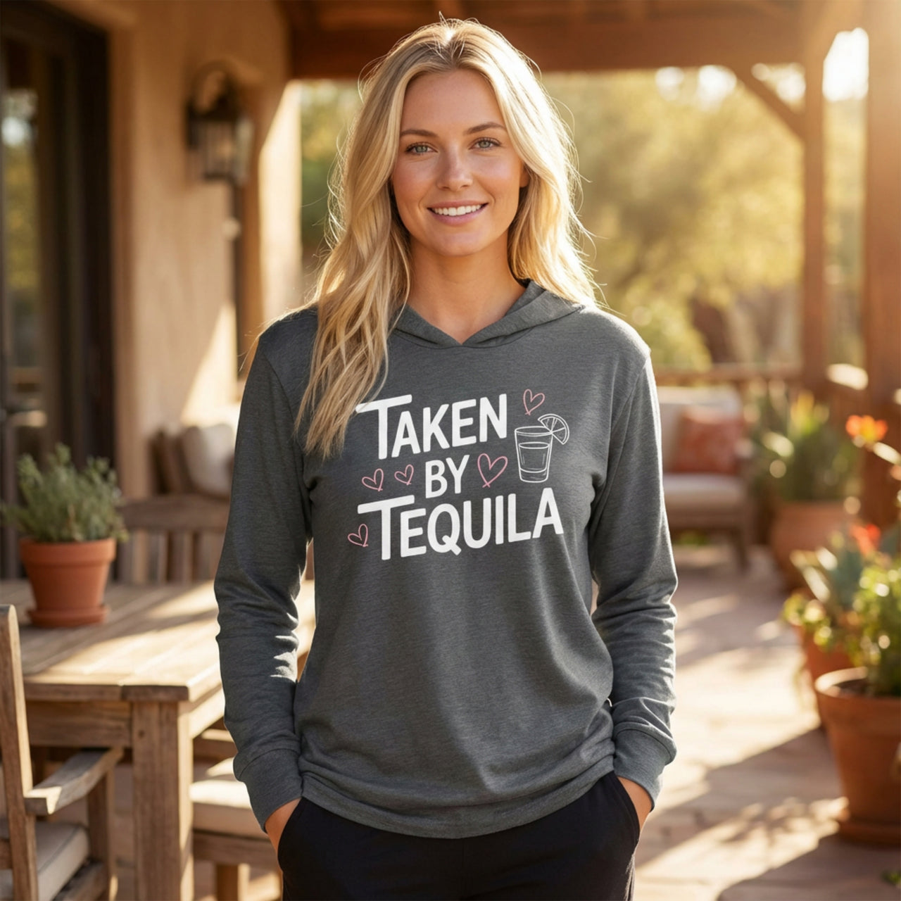 blonde model wearing gray featherweight hoodie with the phrase "Taken By Tequila" with a sketched valentine's hearts and a shot glass with a lime surrounding the phrase to complete the design
