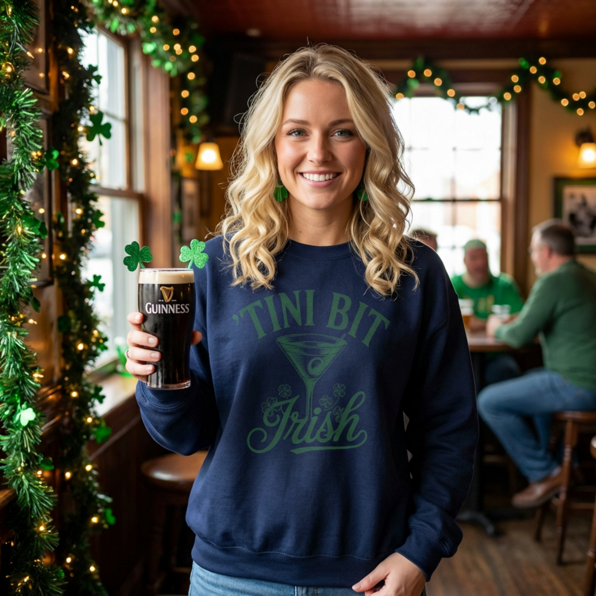 Woman wearing a navy 'Tini Bit Irish' sweatshirt holding a Guinness beer in a festive bar setting funny St Patricks day design