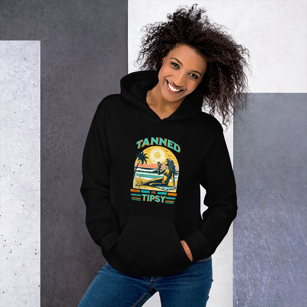 Woman on beach at sunset in our 'Tanned and Tipsy' hoodie, combining vintage charm with beach drinking fun, ideal for cooler evenings.