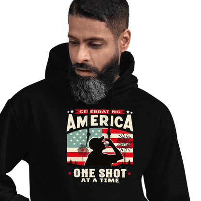 Hoodie with Celebrating America One Shot at a Time text, silhouette of a man drinking a shot, and distressed American flag background. Perfect for 4th of July.