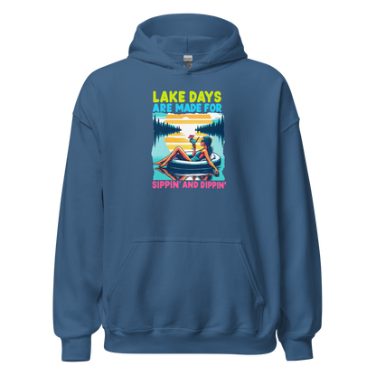 Hoodie with "Lake Days Are Made for Sipping and Dipping," showing a woman on a tube float with a cocktail, lake and sunset scene.