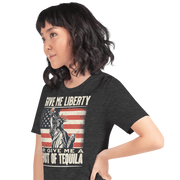 T-shirt with Give Me Liberty or Give Me a Shot of Tequila text, Statue of Liberty holding a shot glass, and distressed American flag background. Perfect for 4th of July.