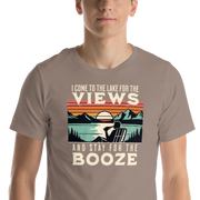 Tee showing "I Come to the Lake for the Views and Stay for the Booze," with a man in a beach chair, lake, and retro sunset.