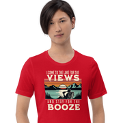 Tee showing "I Come to the Lake for the Views and Stay for the Booze," with a man in a beach chair, lake, and retro sunset.