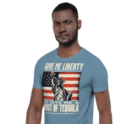 T-shirt with Give Me Liberty or Give Me a Shot of Tequila text, Statue of Liberty holding a shot glass, and distressed American flag background. Perfect for 4th of July.