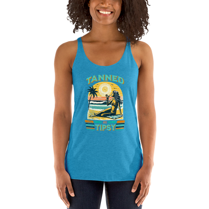 Retro 'Tanned and Tipsy' racerback tank with a woman enjoying a sunset cocktail on the beach, ideal for summer beach parties and day drinking.