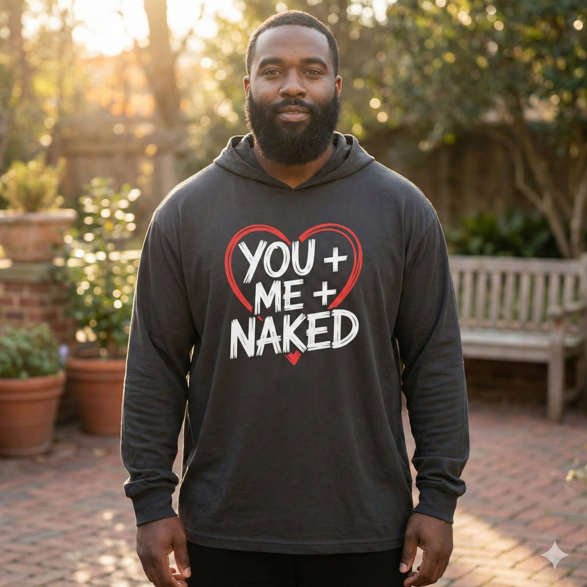 black model wearing black featherweight hoodie with the phrase "You + Me + Naked" with a minimalist sketched valentine's heart surrounding the phrase to complete the design
