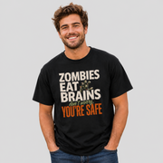 A smiling man wearing a black graphic t-shirt with the text 'ZOMBIES EAT BRAINS don't worry, YOU'RE SAFE' in distressed white and orange lettering, paired with blue jeans, against a solid light gray background.